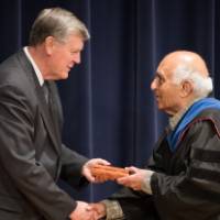 President Emeritus Haas shaking hands and passing over a milestone award to a faculty member.